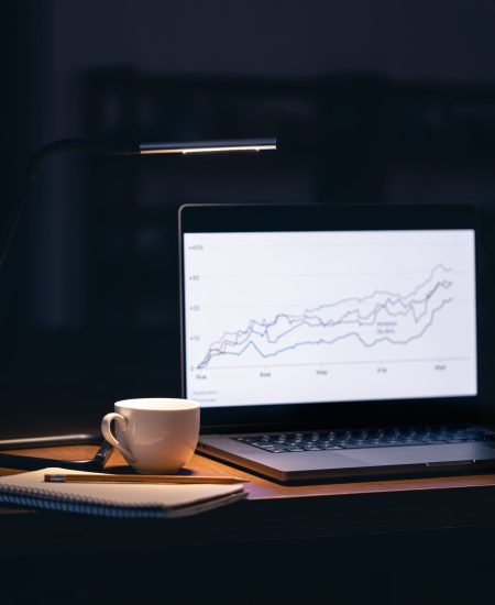 Computer in a dark room with graphs on the screen. Laptop monitor with stock chart at workplace.